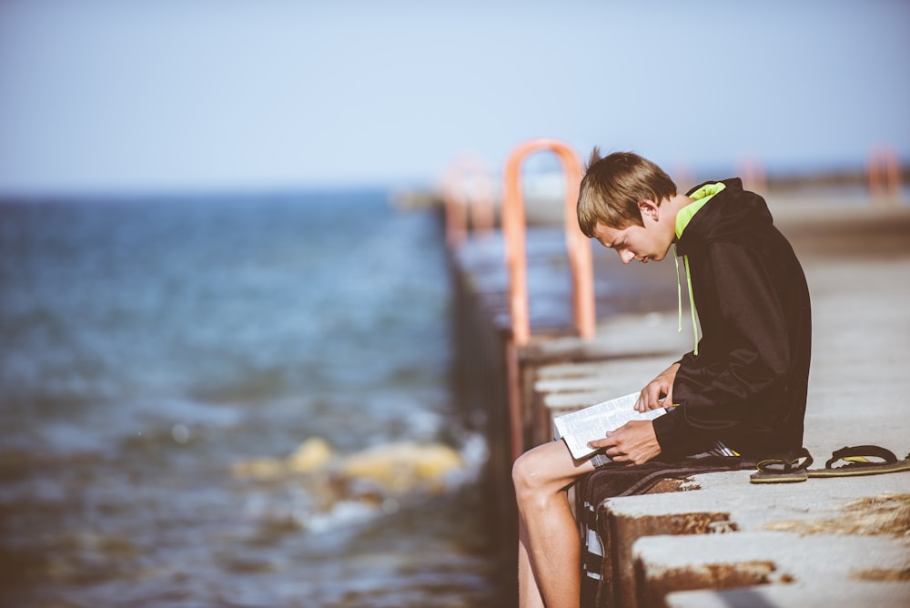 boy sitting on dock while reading