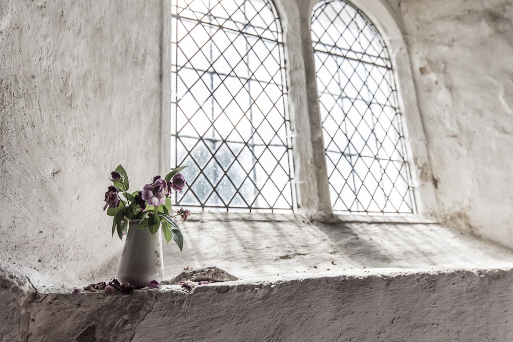 窓際の白い花瓶に緑と紫の花びらの花