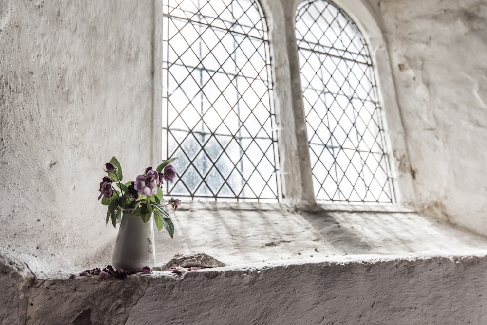 flores de pétalas verdes e roxas no vaso branco perto da janela