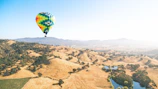 A vibrant hot air balloon floating over rolling green hills.