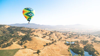 A vibrant hot air balloon floating over rolling green hills.