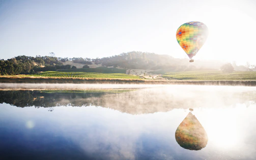 Hot air balloon floating gently above a serene lake reflecting the sky