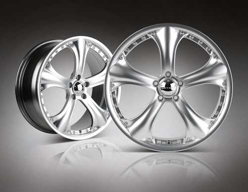 A pair of sleek, metallic alloy wheels with a shiny, polished finish is set against a gradient background. The wheels feature a five-spoke design, and the surface reflects light, emphasizing their smooth and modern appearance.