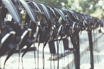 Several black headphones are neatly hung in a row, suspended above a light-colored surface with green foliage visible in the blurred background.