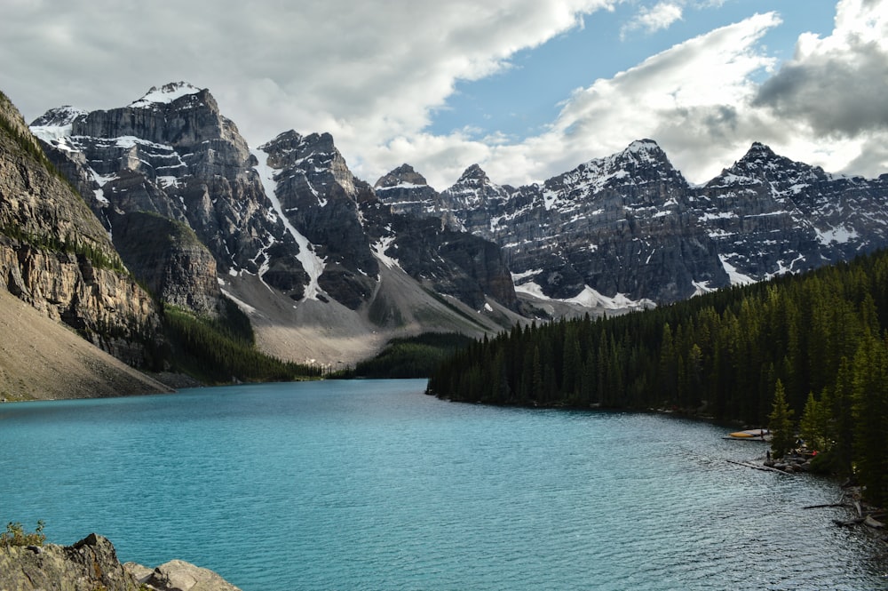 body of water in between snow-capped mountain under white and blue sky