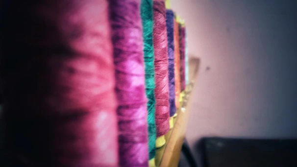 Spools of shiny polyester thread in various pastel shades on a wooden table