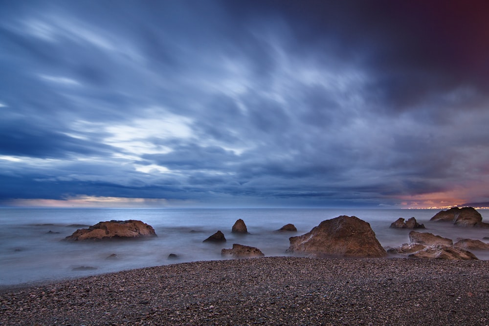 rocks at seashore under clouds