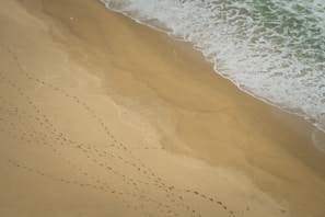 A sandy beach with footprints leading to a sand can placed on the shore.