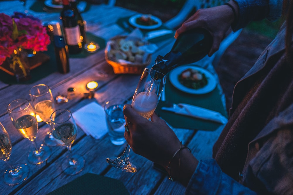 person putting wine on flute glass