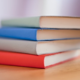 Stack of books with soft green covers on a wooden shelf.