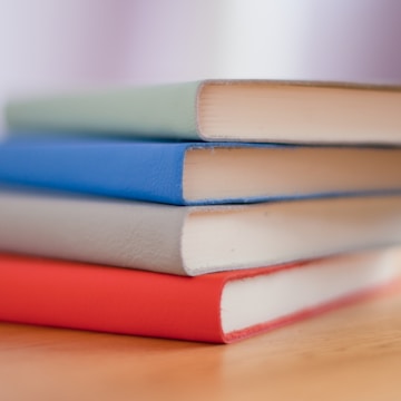 Stack of freshly printed and bound books with colorful covers on a wooden table.