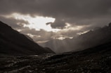 A dramatic landscape of mountains under a cloudy sky with rays of sunlight breaking through