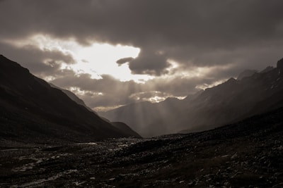 A dramatic landscape of mountains under a cloudy sky with rays of sunlight breaking through