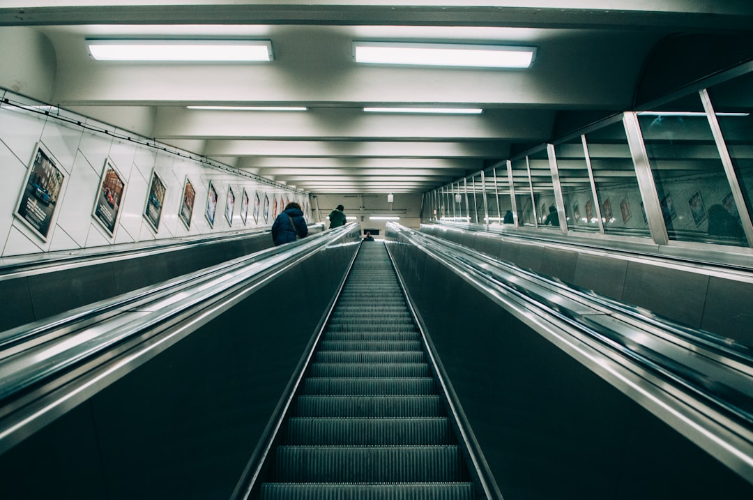 Ascending steep escalator in Stockholm station with posters along the wall and flourescent lights overhead