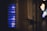 A close-up view of an illuminated apartment intercom system with multiple buttons and labels, each emitting a soft blue glow. The surrounding environment appears dimly lit, creating a contrast between the bright interface and the dark background.