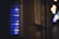 A close-up view of an illuminated apartment intercom system with multiple buttons and labels, each emitting a soft blue glow. The surrounding environment appears dimly lit, creating a contrast between the bright interface and the dark background.