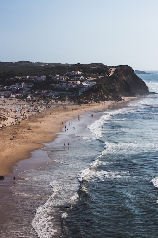 group of people walking on shore beside body of water in Praia do Monte Clérigo Portugal