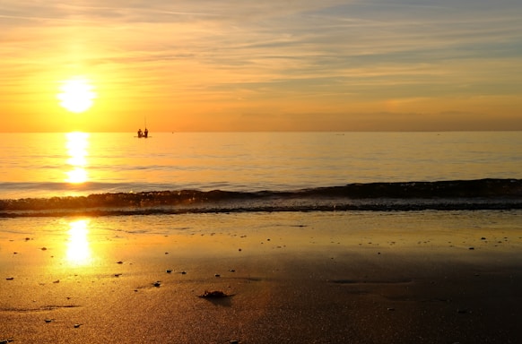 A serene beach sunset with gentle waves and a small boat anchored near the shore.
