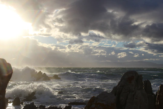 Dramatic waves breaking against dark rocky cliffs with a bright sky overhead.