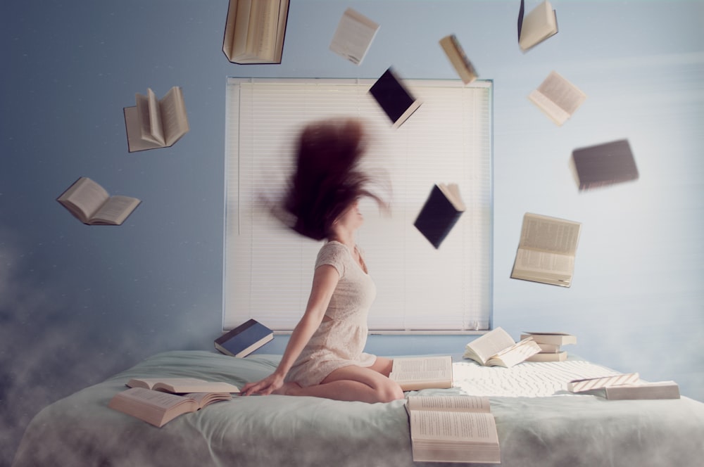 Mujer sentada en la cama con libros voladores