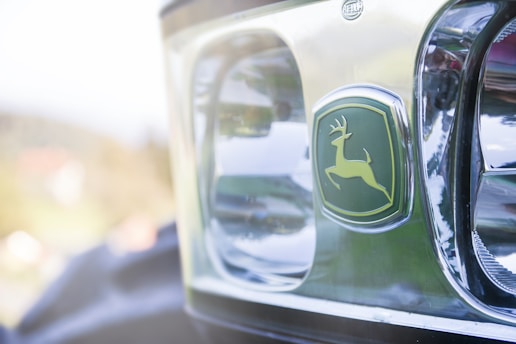 Close-up view of a vehicle's front with a chrome finish and a distinctive logo featuring a jumping deer, set against a green background.