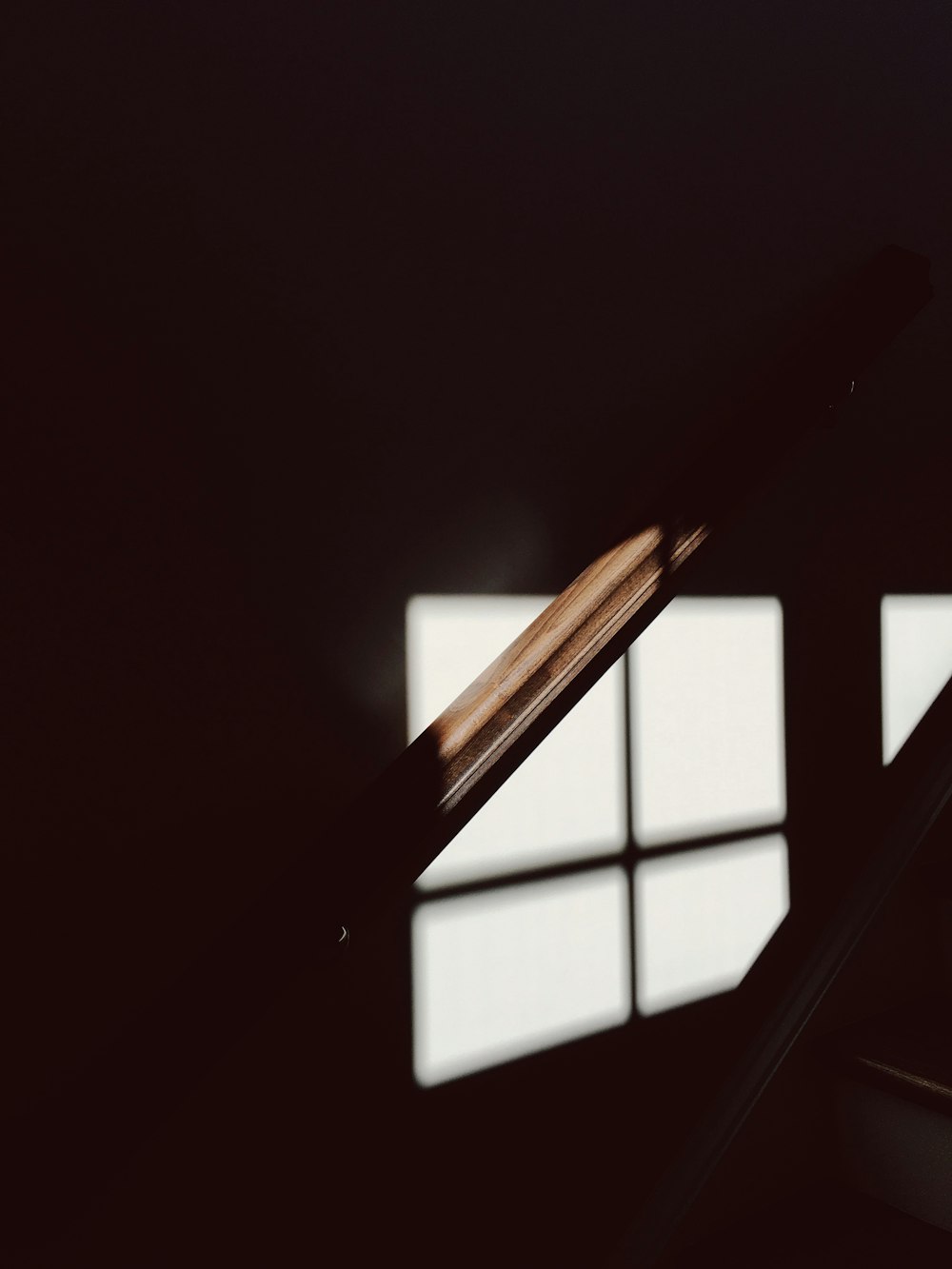 A dim shot of a wooden bannister illuminated by faint light from the window