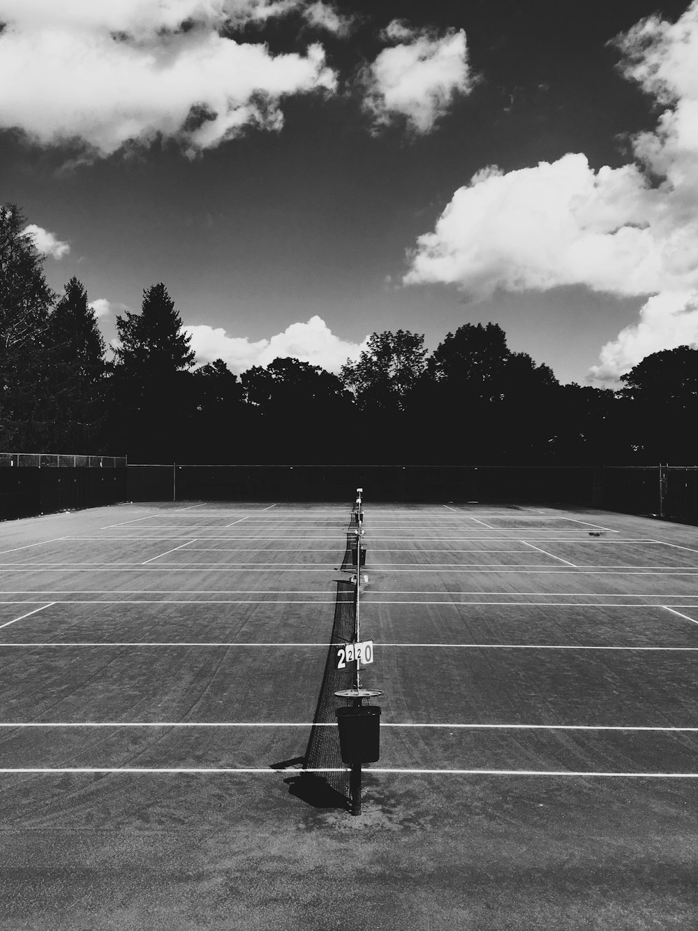 A look down the middle of a tennis net with a darkened background on a partially cloudy day.