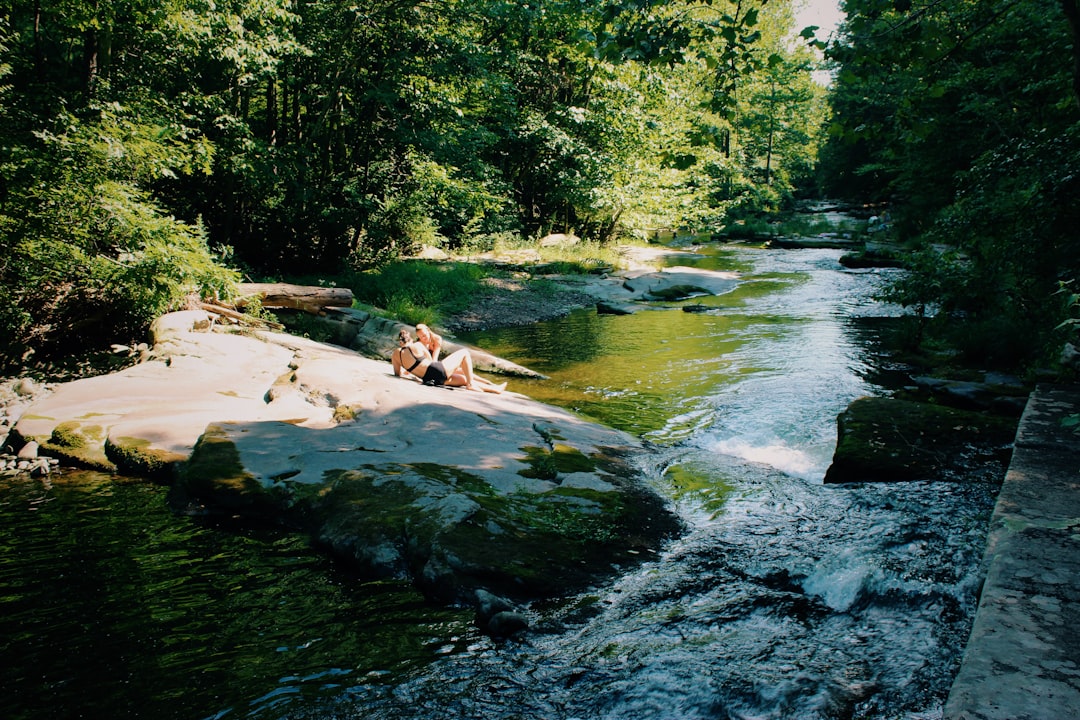 two women sitting on rock beside river
