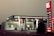 A Lukoil gas station with a modern design features prominently, displaying fuel prices on a tall, illuminated sign. The station includes a minimarket and several fuel pumps under a canopy. The lighting suggests a dusk or dawn setting, casting a soft ambient glow.