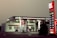 A Lukoil gas station with a modern design features prominently, displaying fuel prices on a tall, illuminated sign. The station includes a minimarket and several fuel pumps under a canopy. The lighting suggests a dusk or dawn setting, casting a soft ambient glow.
