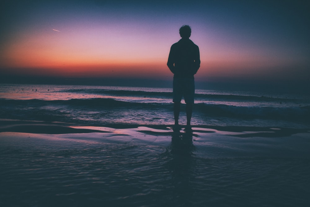 man standing on seashore during sunset