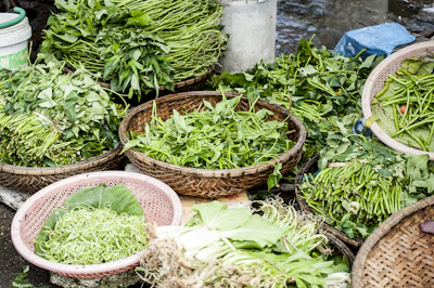 Bright green vegetables and seeds neatly arranged in traditional Thai market baskets.