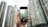 A hand holding a smartphone, which is capturing an image of tall skyscrapers. The buildings are modern and densely packed, and the phone's screen shows a live view of the architecture.