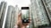 A hand holding a smartphone, which is capturing an image of tall skyscrapers. The buildings are modern and densely packed, and the phone's screen shows a live view of the architecture.