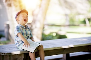 boy sitting outdoor, laughing and holding a book