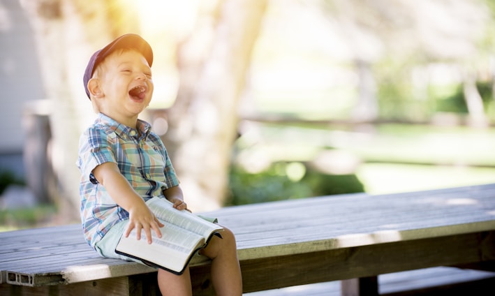 boy sitting on bench while holding a book