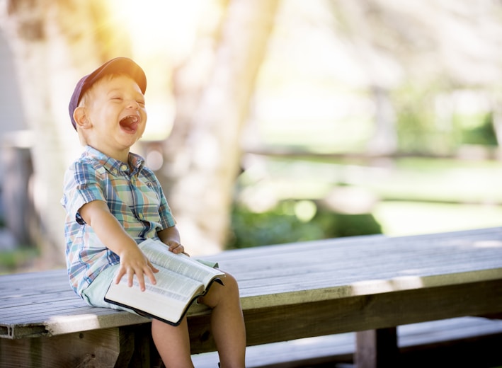 boy sitting on bench while holding a book