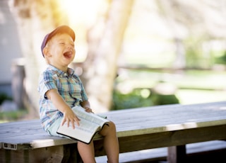 boy sitting on bench while holding a book