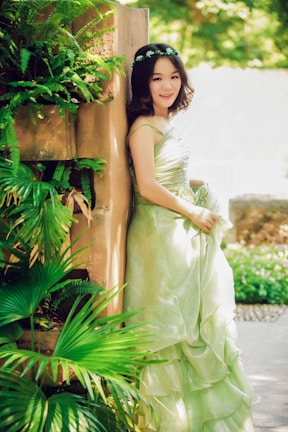 A woman in a flowing, patterned dress accessorized with a delicate necklace, smiling softly in natural sunlight.