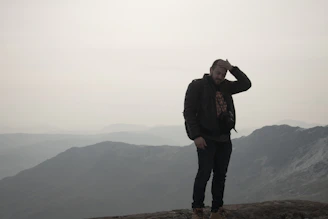 A person standing on a mountain peak, looking thoughtfully at the horizon.