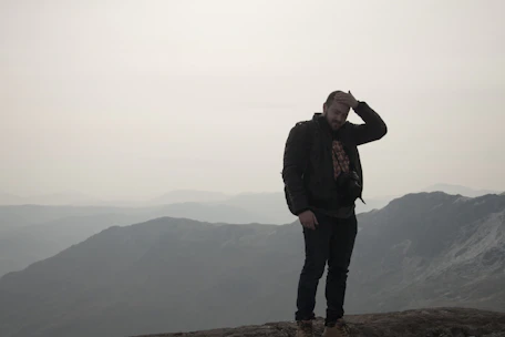 A person standing on a mountain peak, looking thoughtfully at the horizon.