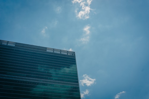 A modern office building with reflective glass windows is positioned against a clear blue sky dotted with a few white clouds.