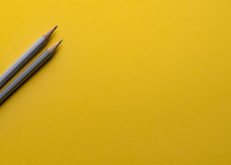 two gray pencils on yellow surface