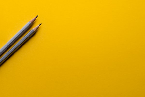 A picture of two pencils on a yellow background.