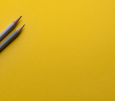 two gray pencils on yellow surface