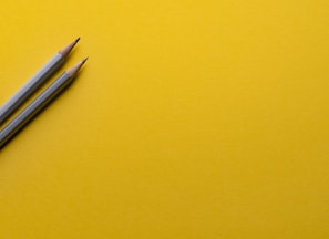 two gray pencils on yellow surface