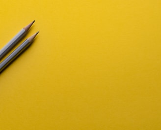 two gray pencils on yellow surface