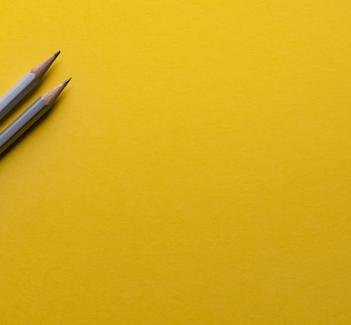 two gray pencils on yellow surface