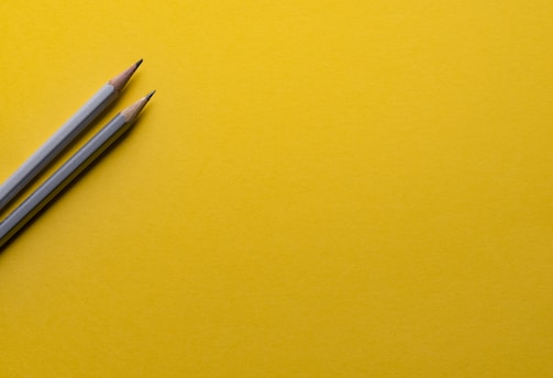 two gray pencils on yellow surface