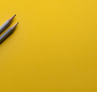 two gray pencils on yellow surface